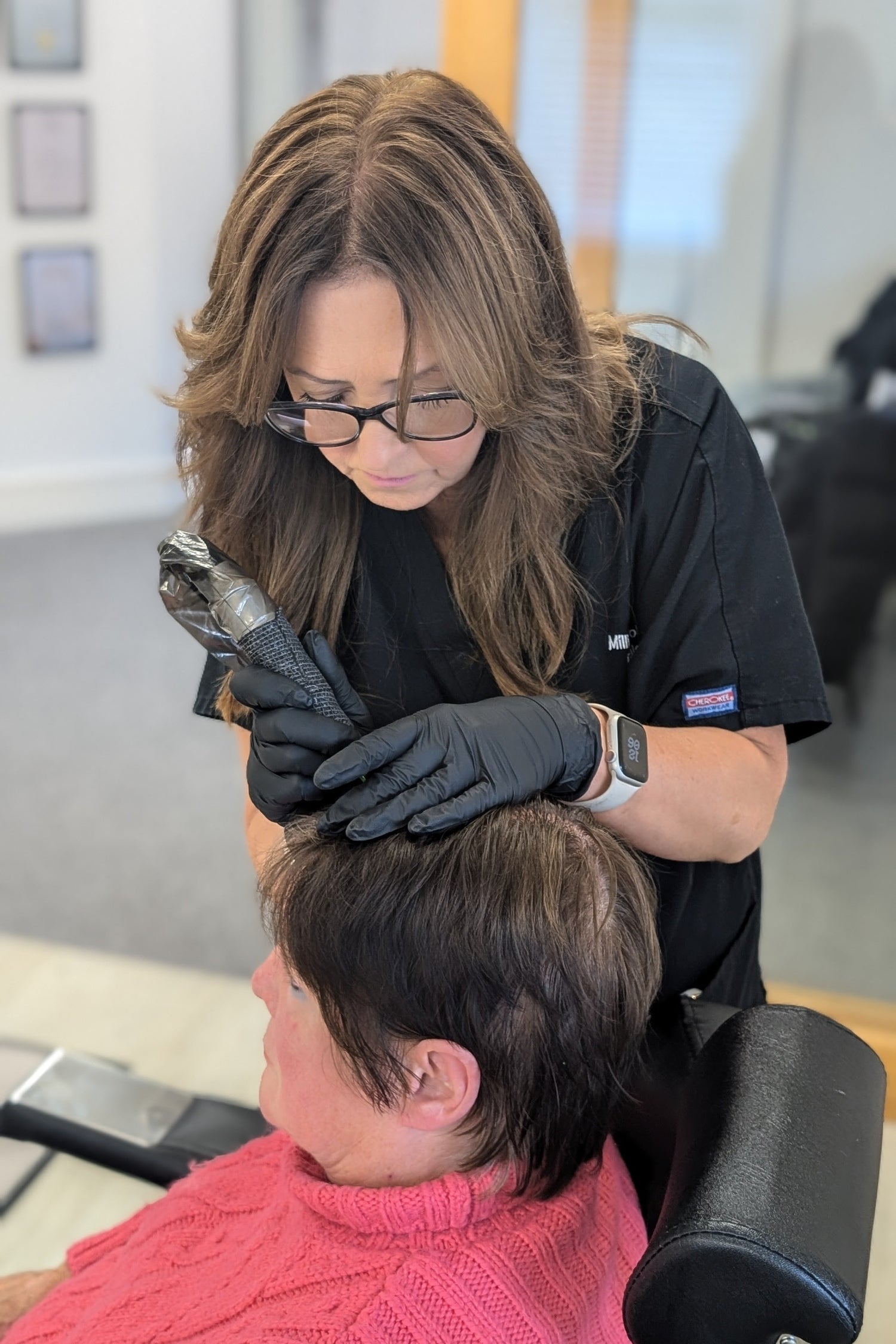 Practitioner performing scalp micropigmentation on female client in a professional clinic setting with gloves and treatment device